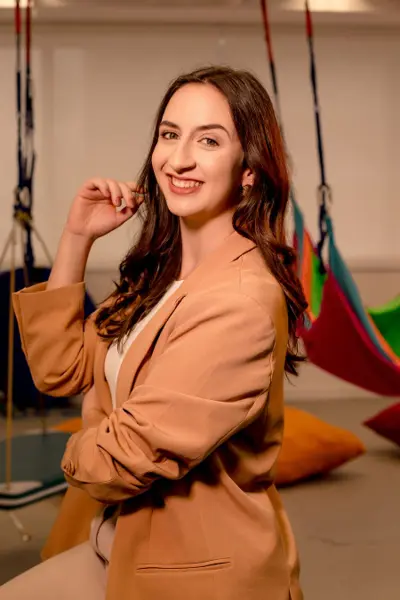 Ana Carolina Ricardo sorrindo, em uma sala de terapia ocupacional com balanços suspensos ao fundo