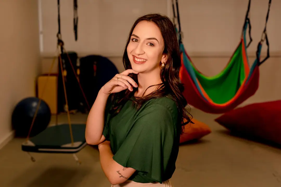 Ana Carolina Ricardo em sua sala de atendimento, com balanços e almofadas coloridas ao fundo